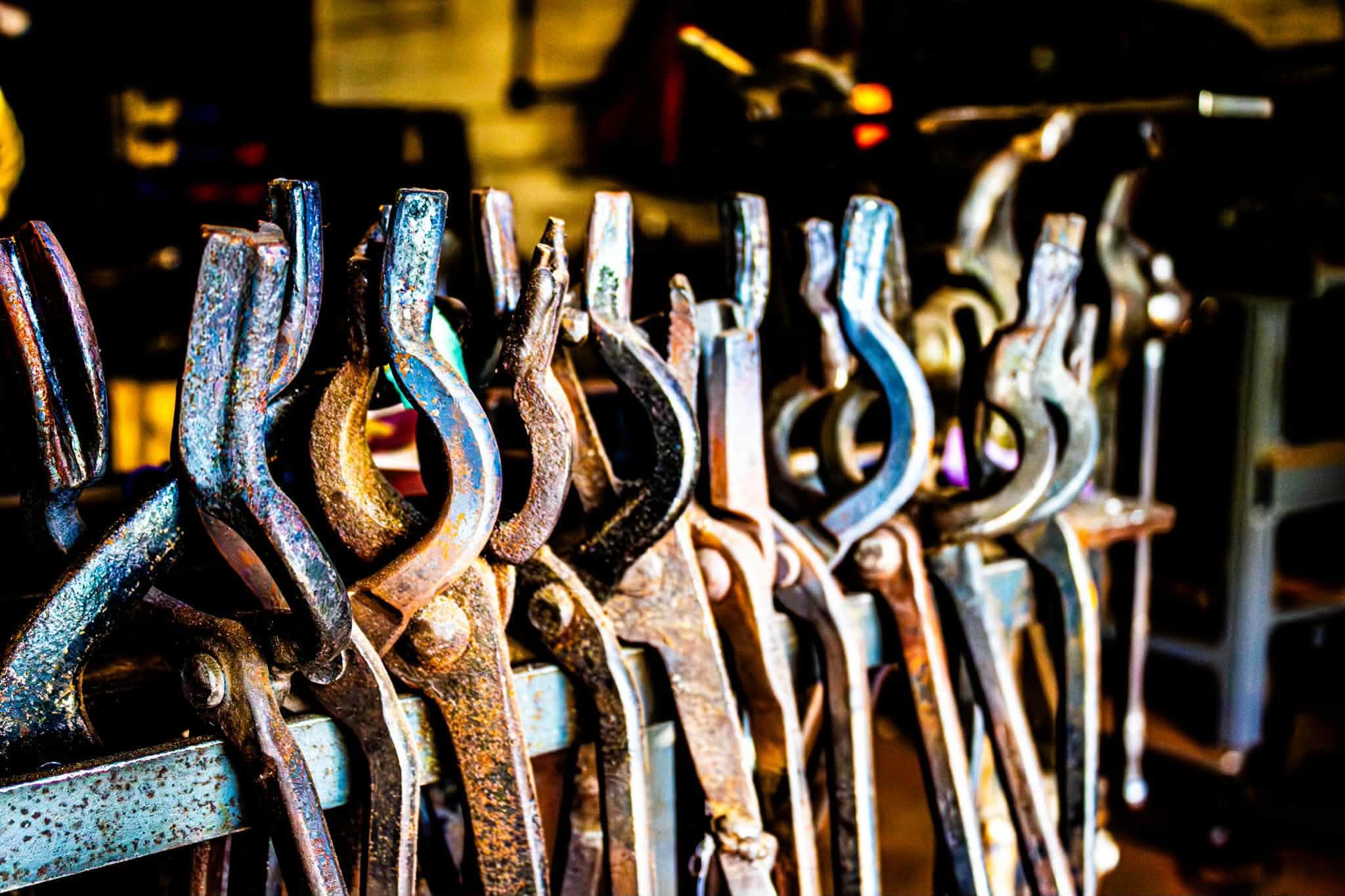 A row of forging tongs hanging from a rack in the shop