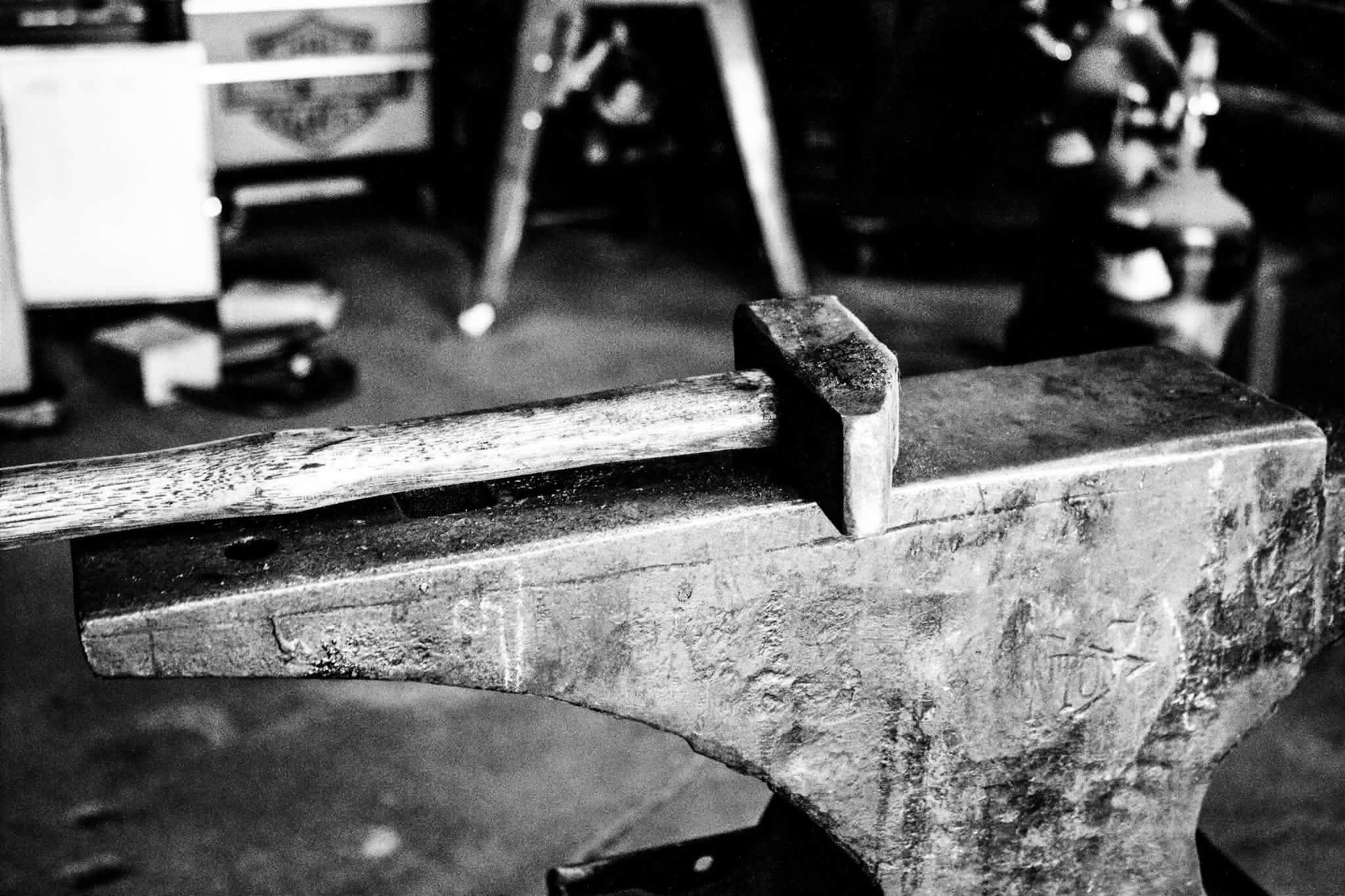 A hand hammer resting on the face of an anvil, in black and white
