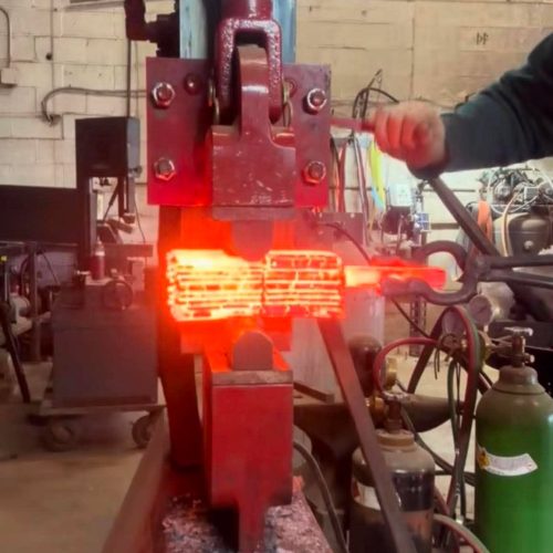 A stack of pattern-welded steel glowing red as the hydraulic press squeezes the billet together