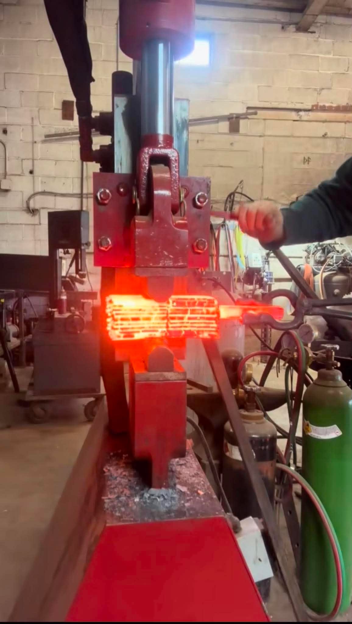 A stack of pattern-welded steel glowing red as the hydraulic press squeezes the billet together