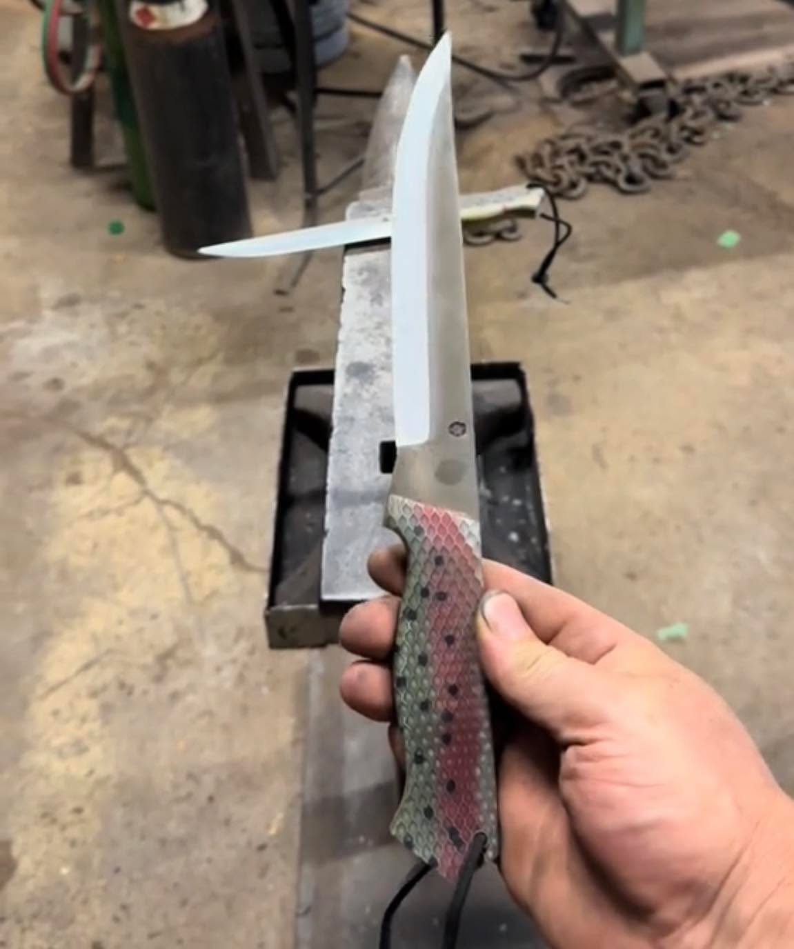 A field knife with a bright satin blade and a patterned handle, held in front of the anvil